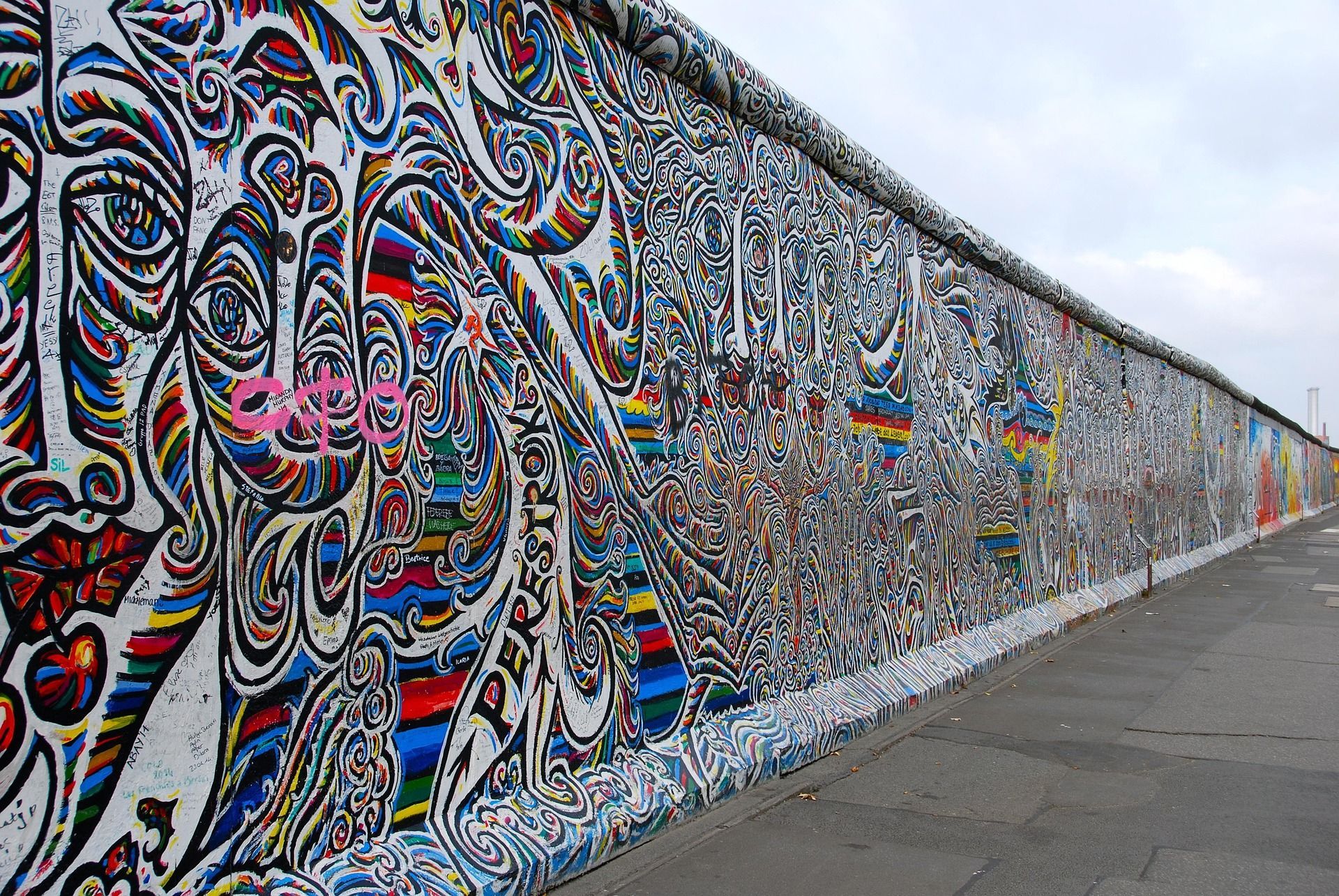 Un long mur de béton, recouvert de graffitis colorés et complexes, s'étend le long d'un trottoir sous un ciel gris.