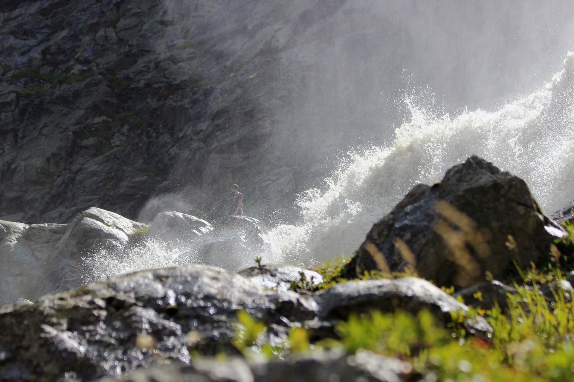 Eine Person steht auf einem großen Felsen neben dem gewaltigen Sprühnebel und der Gischt eines rauschenden Wasserfalls.