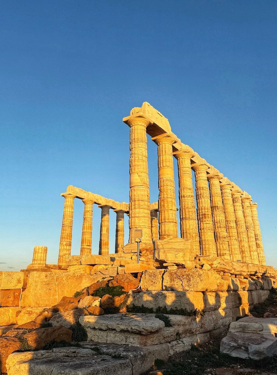 La luce dorata del sole illumina le colonne in pietra di un'antica rovina di tempio contro un cielo azzurro e sereno.