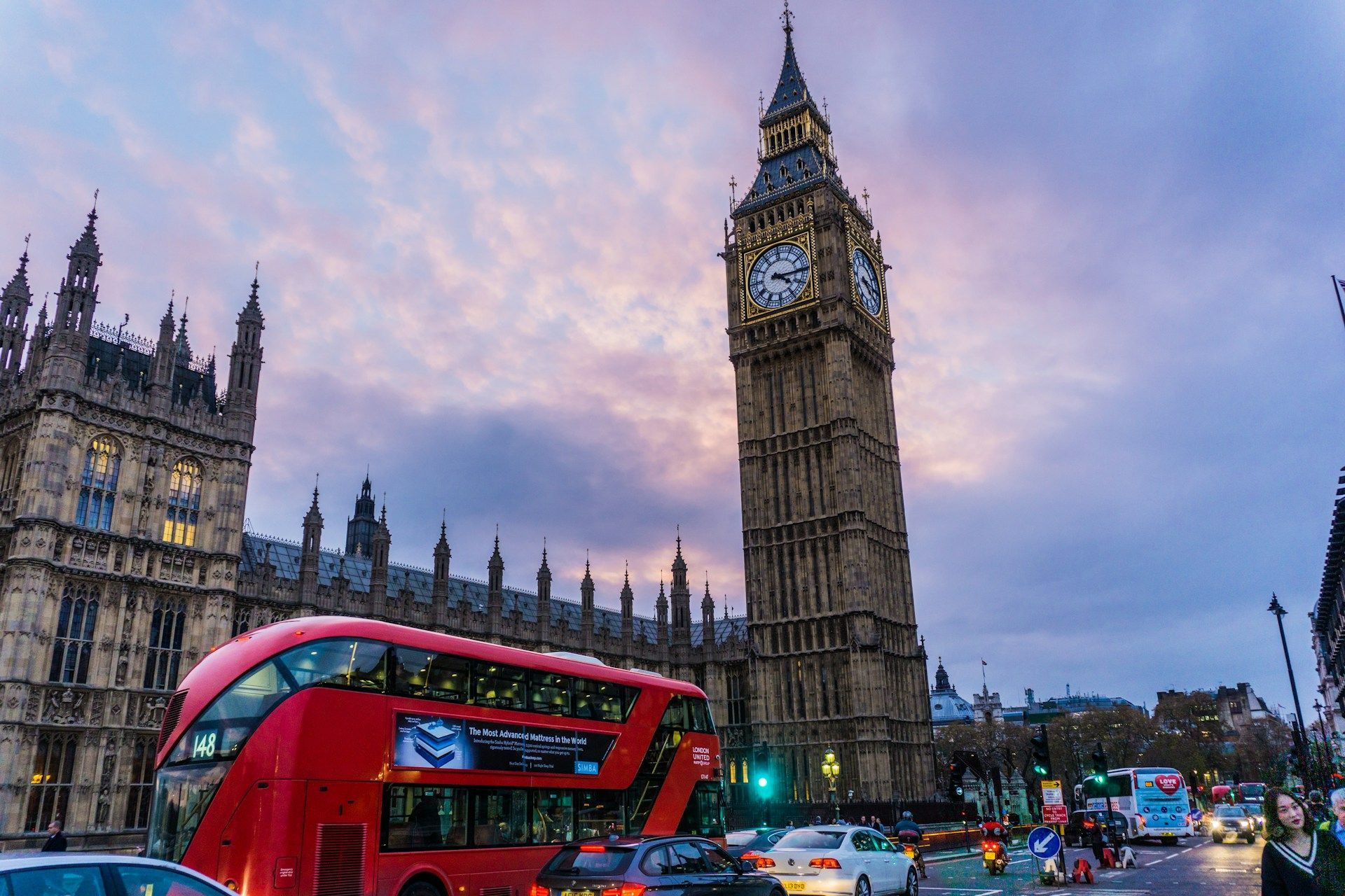 Un bus rouge à impériale passe devant la tour de l'horloge de Big Ben et le Parlement sous un ciel nuageux au crépuscule.