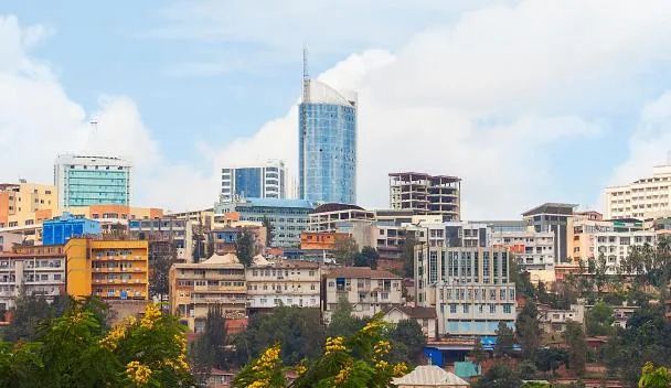 Un paysage urbain dense avec un gratte-ciel moderne en verre et d'autres bâtiments sur une colline sous un ciel partiellement nuageux.