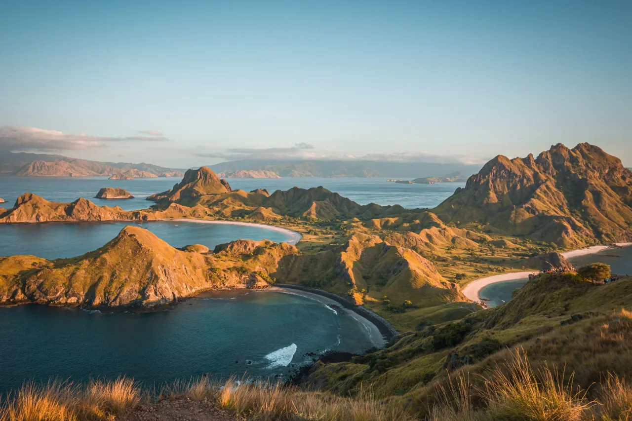 Una vista panoramica di un paesaggio costiero con isole aspre ed erbose, spiagge sabbiose e un mare blu calmo sotto un cielo sereno.