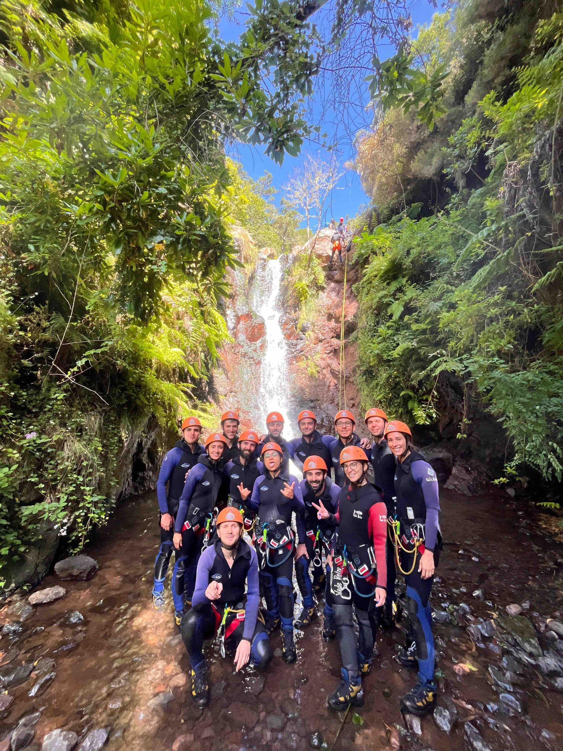 Un gruppo WeRoad in viaggio, con attrezzatura completa da canyoning, in posa in un torrente roccioso alla base di una cascata.