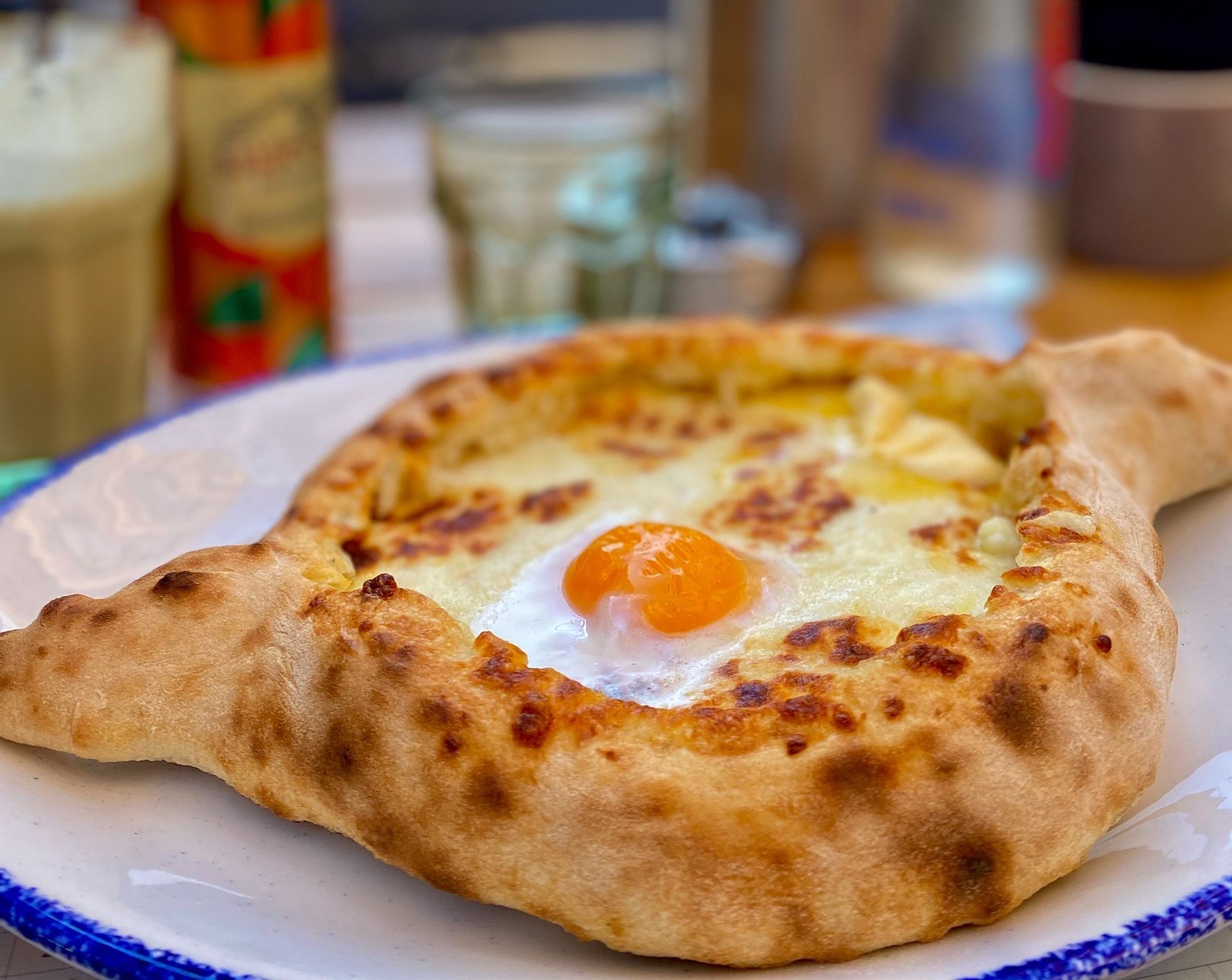Primo piano di un Khachapuri Adjaruli, un pane a forma di barca ripieno di formaggio fuso e un tuorlo d'uovo crudo, su un piatto.
