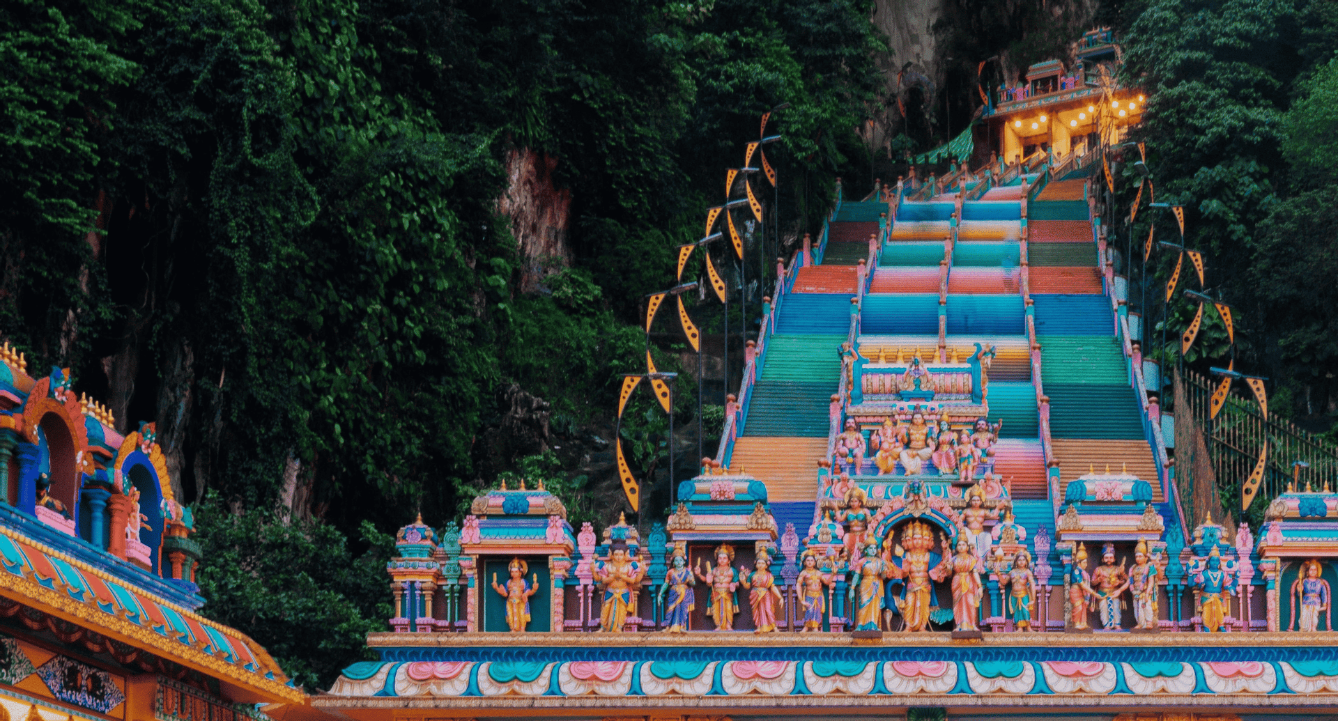 Una lunga e colorata scalinata conduce su un ripido pendio ricoperto di giungla verso l'ingresso di un tempio ornato.