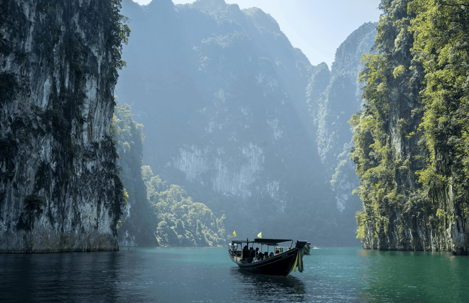 Un viaggio di gruppo WeRoad su una long-tail boat galleggia su acque calme tra imponenti scogliere calcaree coperte da una vegetazione lussureggiante.