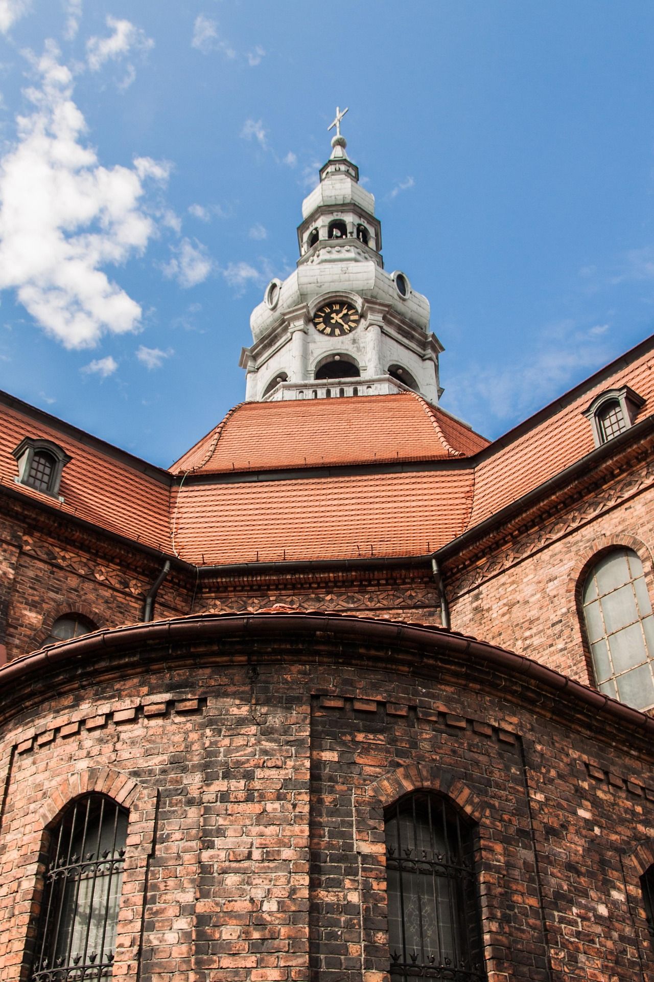 Un'inquadratura dal basso di una chiesa storica in mattoni, con un tetto di tegole rosse e una torre dell'orologio, su un cielo azzurro con nuvole.