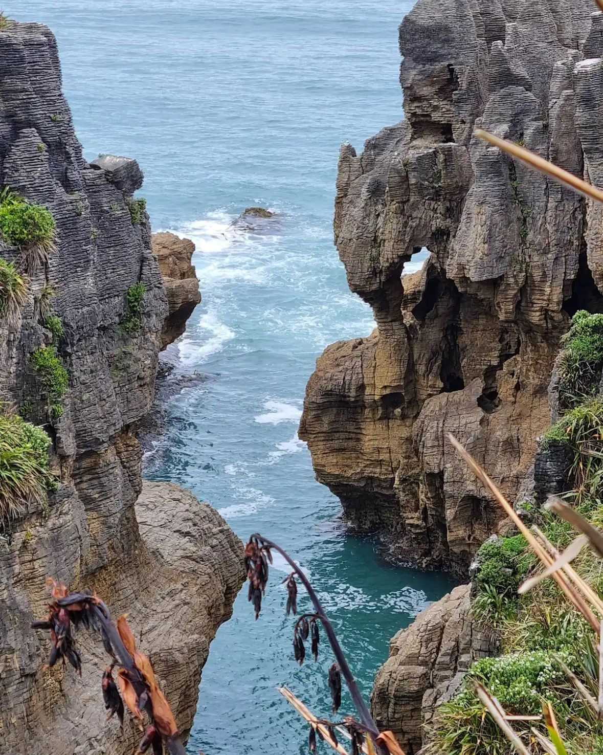 Layered rock cliffs form a narrow inlet with turquoise ocean water flowing between them, as seen from a high vantage point.