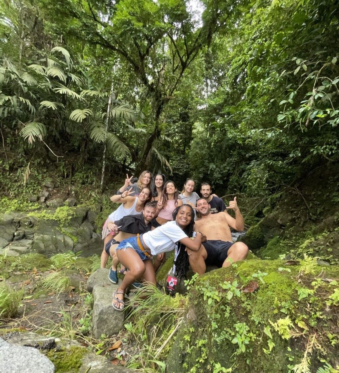 A WeRoad group trip smiles and poses for a photo on mossy rocks in a dense green jungle.