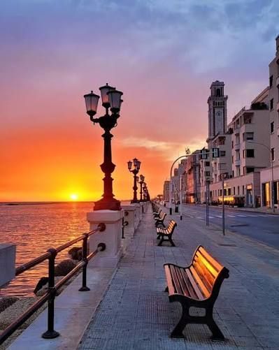 Una passeggiata sul lungomare con panchine e lampioni al tramonto sul mare.