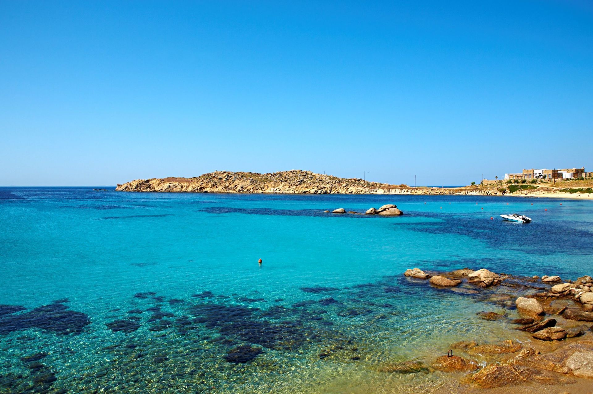 Una baia costiera con acqua cristallina turchese, una costa rocciosa e una piccola barca che galleggia sotto un cielo blu.