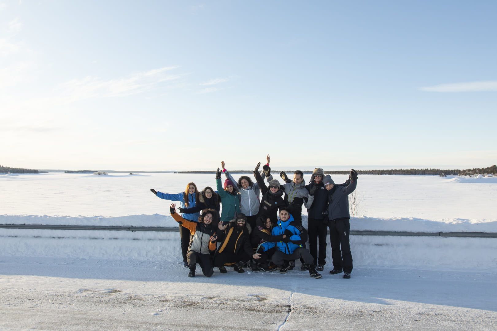 Un gruppo WeRoad in viaggio, con abbigliamento invernale, in posa per una foto in un vasto paesaggio innevato sotto un cielo sereno.