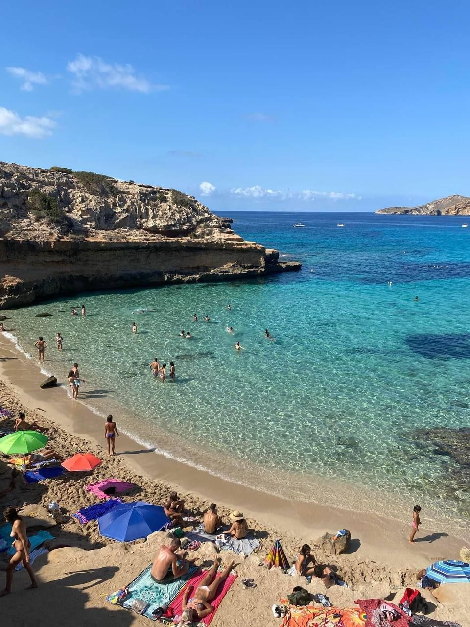 Vista dall'alto di una spiaggia in una cala, con persone che nuotano in acque turchesi cristalline e si rilassano sulla sabbia.