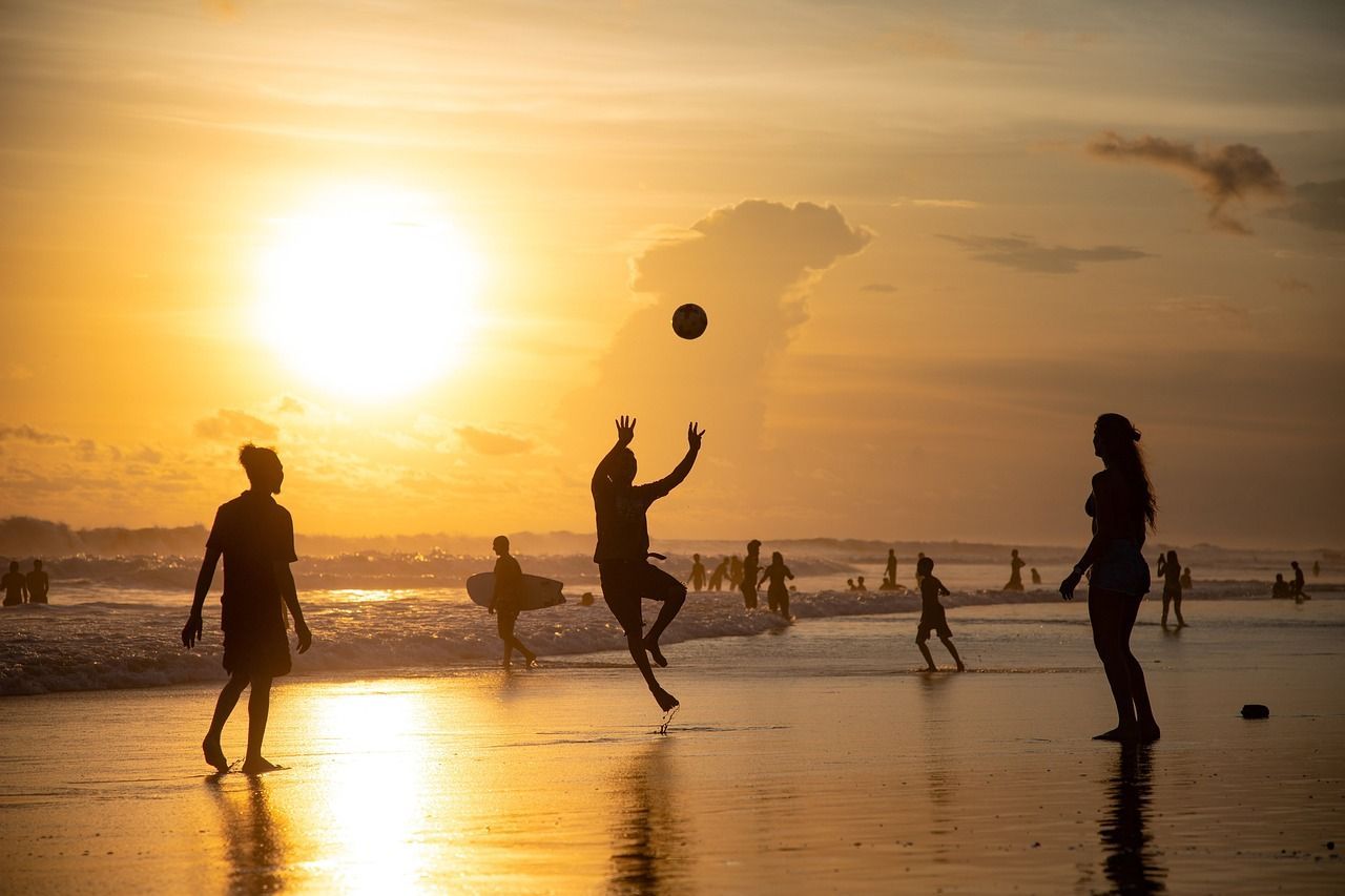 Un gruppo WeRoad in silhouette su una spiaggia al tramonto, con una persona che salta per afferrare una palla.