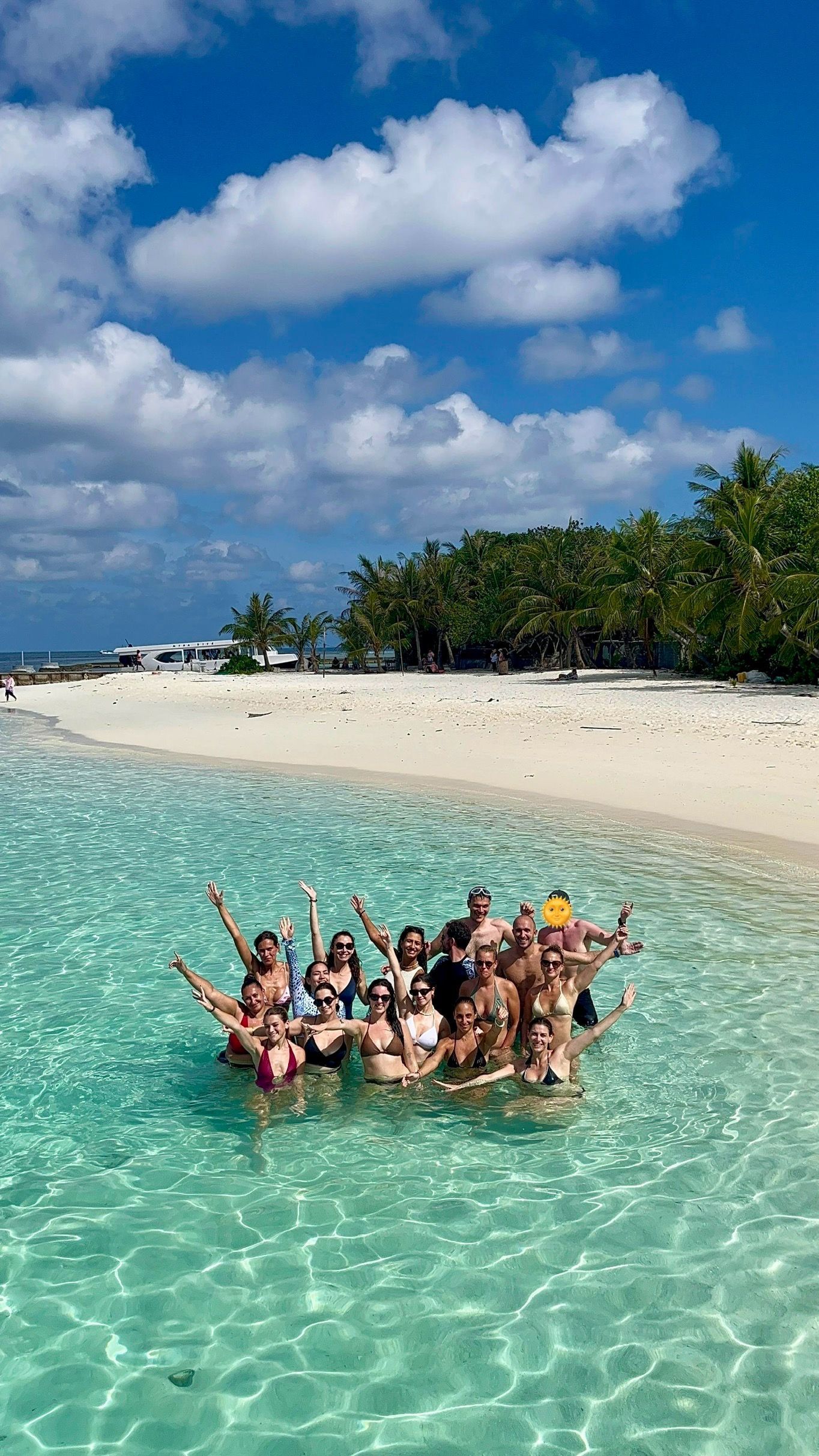 Un gruppo WeRoad in posa e sorridente in acque basse e turchesi, vicino a una spiaggia di sabbia bianca orlata di palme.