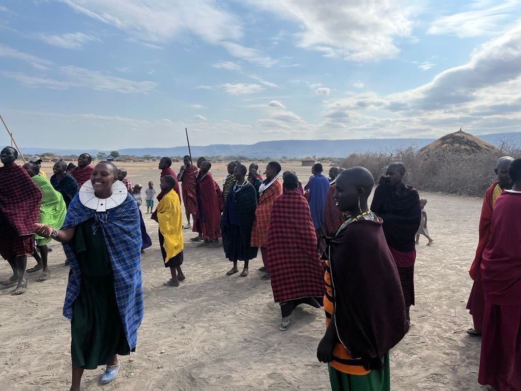 Un gruppo di Maasai, con indosso colorate vesti tradizionali e gioielli, si riunisce nel loro villaggio in un paesaggio arido e aperto.