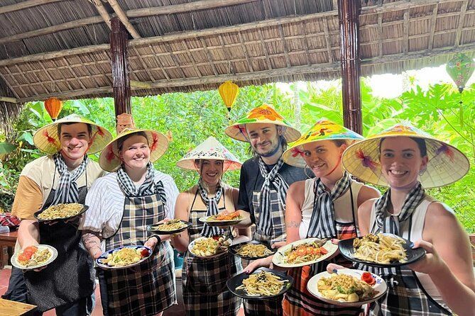 Un gruppo WeRoad di sei persone che indossano cappelli conici e grembiuli, sorridono e tengono piatti di cibo a un corso di cucina.