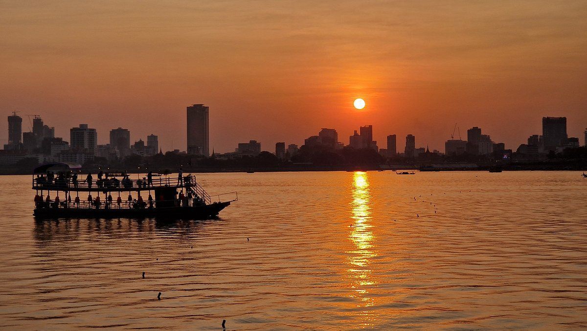 Un viaggio di gruppo WeRoad su un battello a due piani naviga sull'acqua al tramonto, con lo skyline di una città in silhouette sullo sfondo.