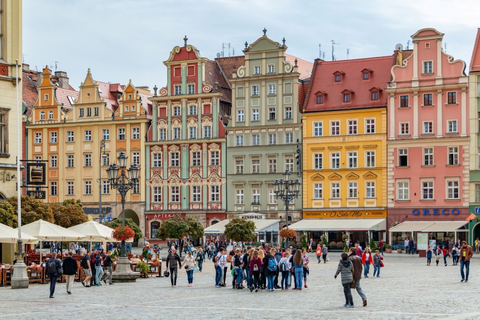 Eine WeRoad Gruppenreise steht auf einem großen Kopfsteinpflasterplatz vor einer Reihe farbenfroher, historischer Gebäude im europäischen Stil.