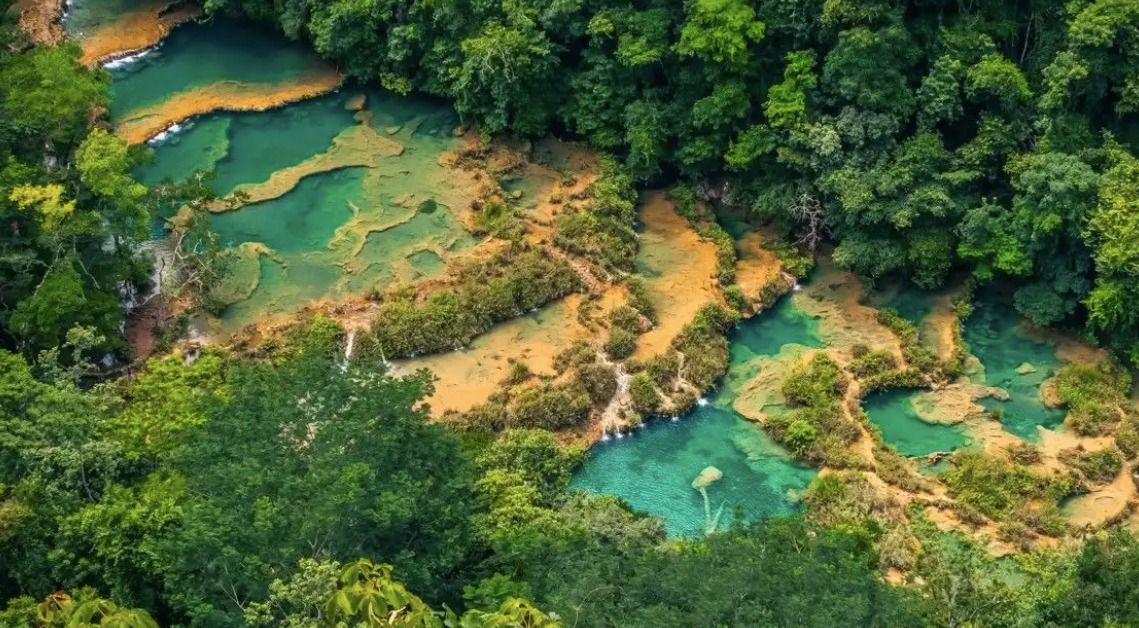 Una vista aerea di piscine terrazzate di acqua turchese e cascate circondate da una foresta lussureggiante e verde.