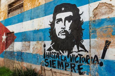 Un mural de arte callejero en una pared desgastada que representa al Che Guevara sobre una bandera cubana con la frase 'Hasta la Victoria Siempre'.