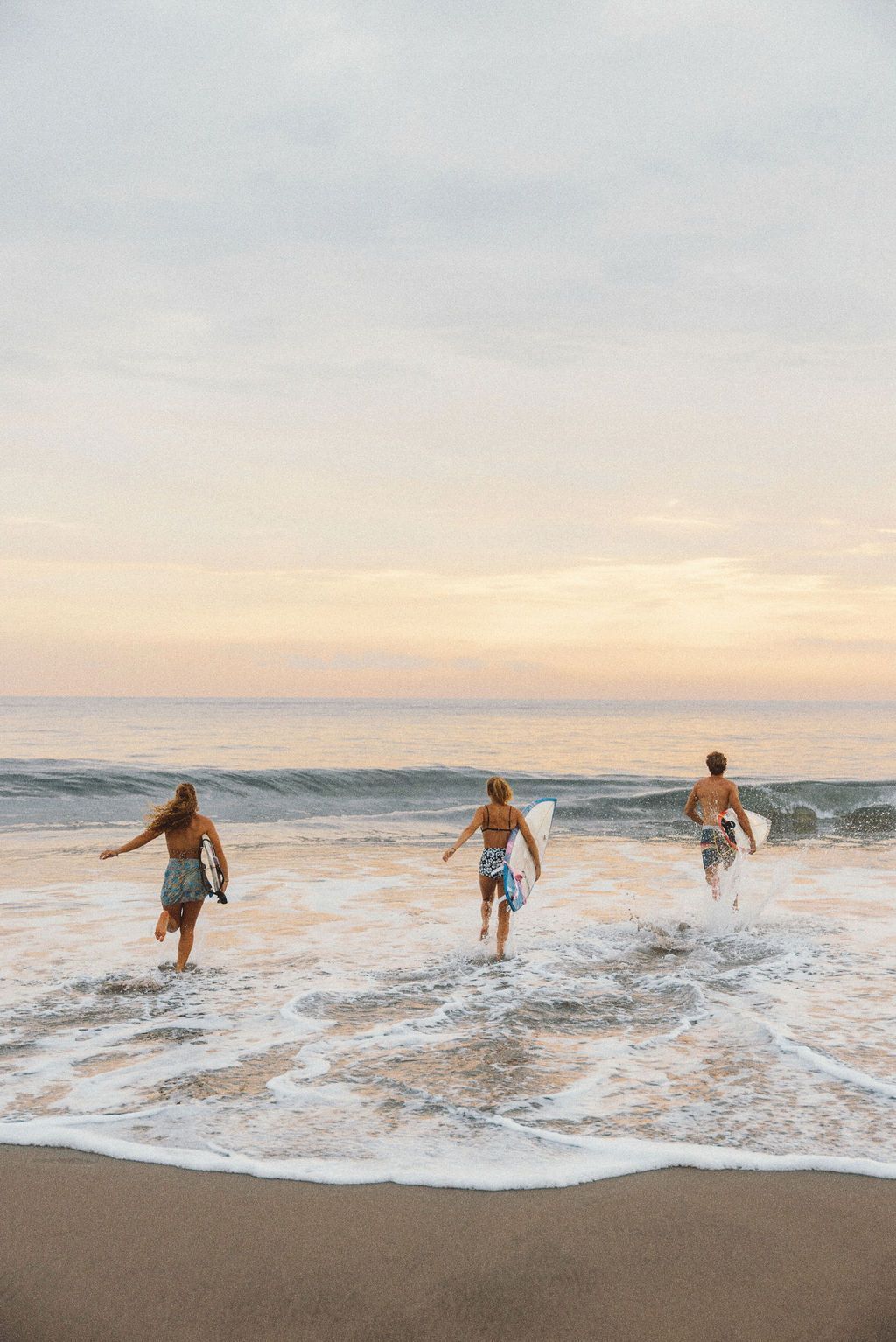 Un viaggio di gruppo WeRoad con tre surfisti che corrono nell'oceano con le loro tavole da surf all'alba.