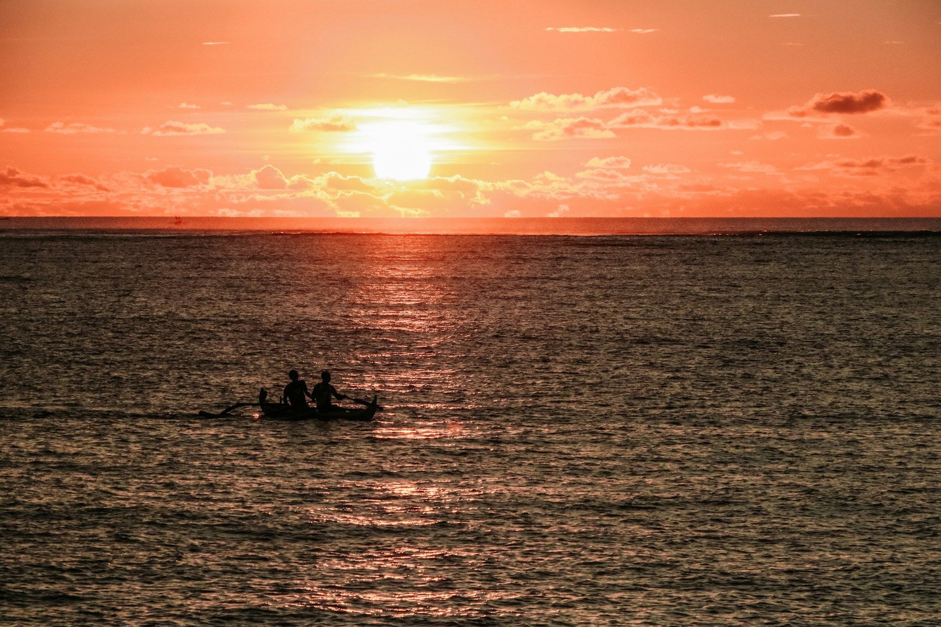 Silhouette di due persone in barca sull'oceano durante un vibrante tramonto arancione.