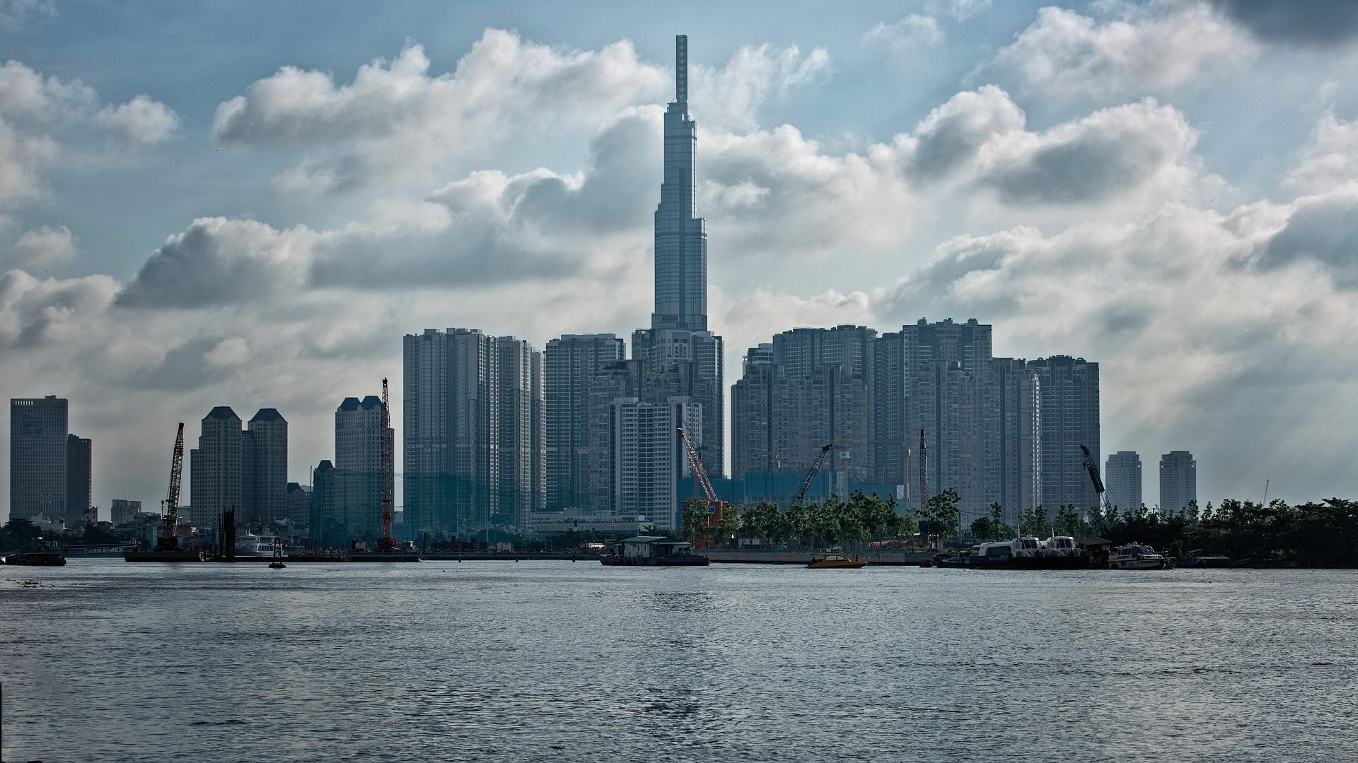 Uno skyline moderno con un grattacielo imponente, visto da oltre uno specchio d'acqua sotto un cielo parzialmente nuvoloso.