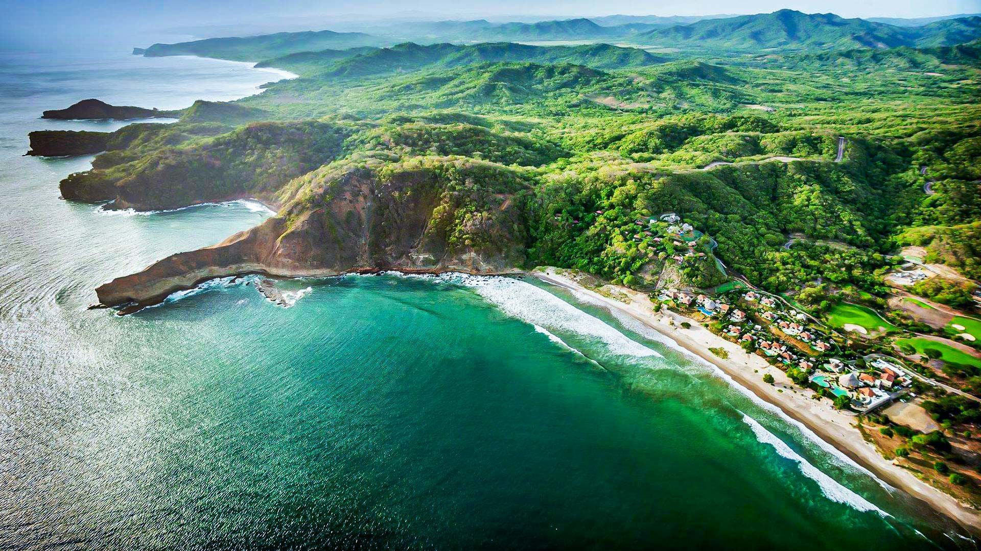 Veduta aerea di una vibrante costa verde con acqua turchese che lambisce una spiaggia sabbiosa e scogliere.
