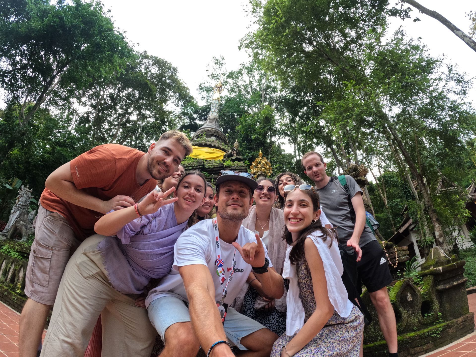 Un gruppo WeRoad in posa per un selfie davanti a uno stupa di pietra circondato da alberi rigogliosi.