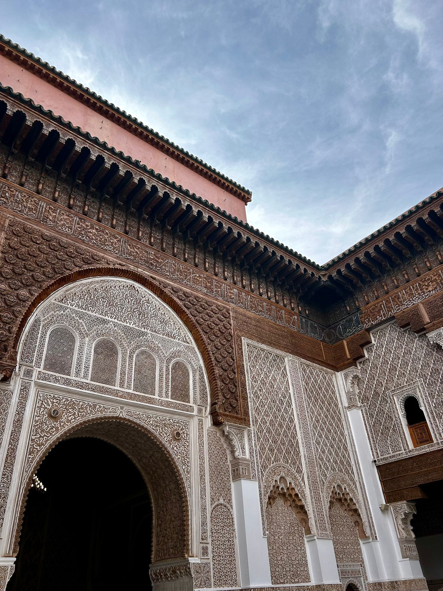 Vista en contrapicado de un patio de edificio ornamentado, con intrincadas tallas de madera y yeso en las paredes y arcos, bajo un cielo nublado.