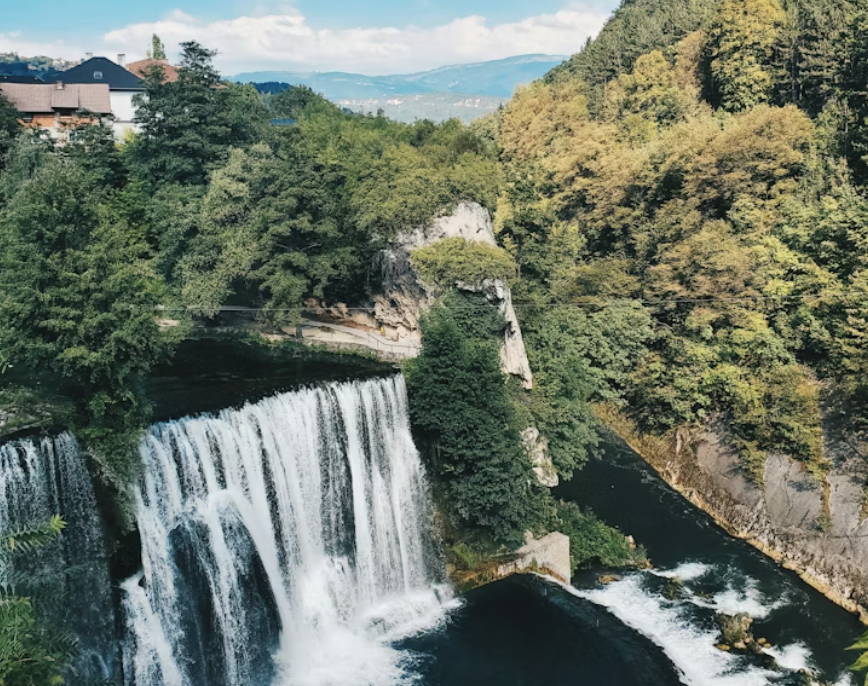 Une grande cascade se jette dans une rivière, entourée d'une forêt verdoyante, avec des maisons à flanc de colline en arrière-plan.