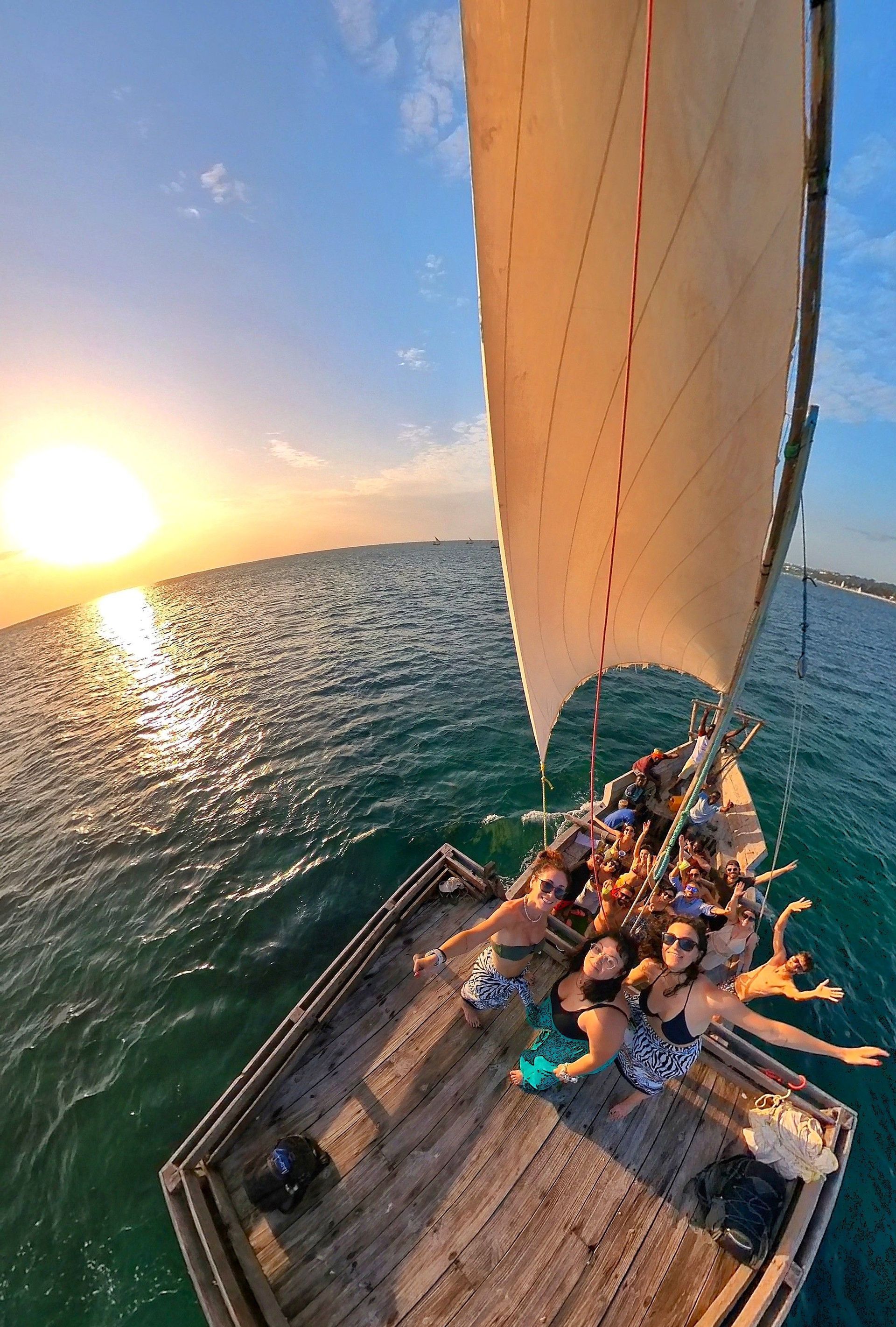 Un groupe WeRoad prend une photo en plongée sur un voilier en bois, naviguant sur l'océan au coucher du soleil.