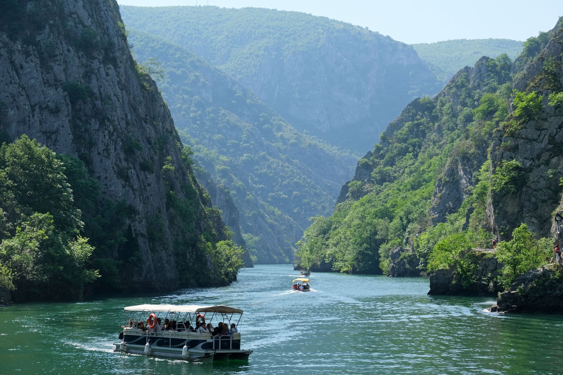 Eine WeRoad-Gruppenreise auf Ausflugsbooten, die an einem sonnigen Tag durch eine Flussschlucht mit steilen, bewaldeten Klippen gleitet.