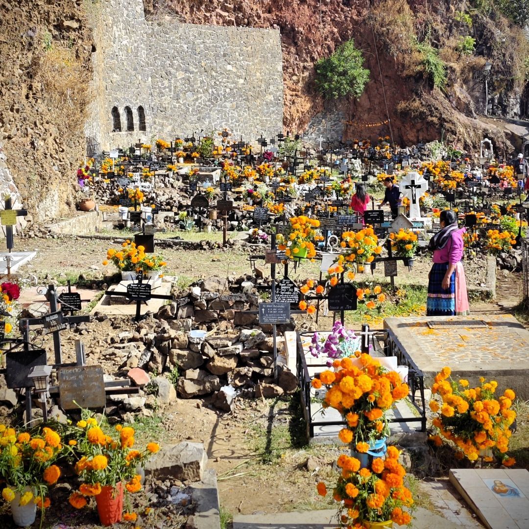 Ein Hangfriedhof mit zahlreichen Gräbern und Kreuzen, die für ein Fest mit leuchtend orangefarbenen Ringelblumen geschmückt sind.
