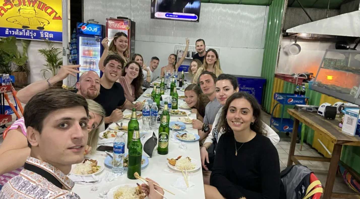 Un grand groupe WeRoad sourit pour une photo, attablé à une longue table dans un restaurant décontracté.