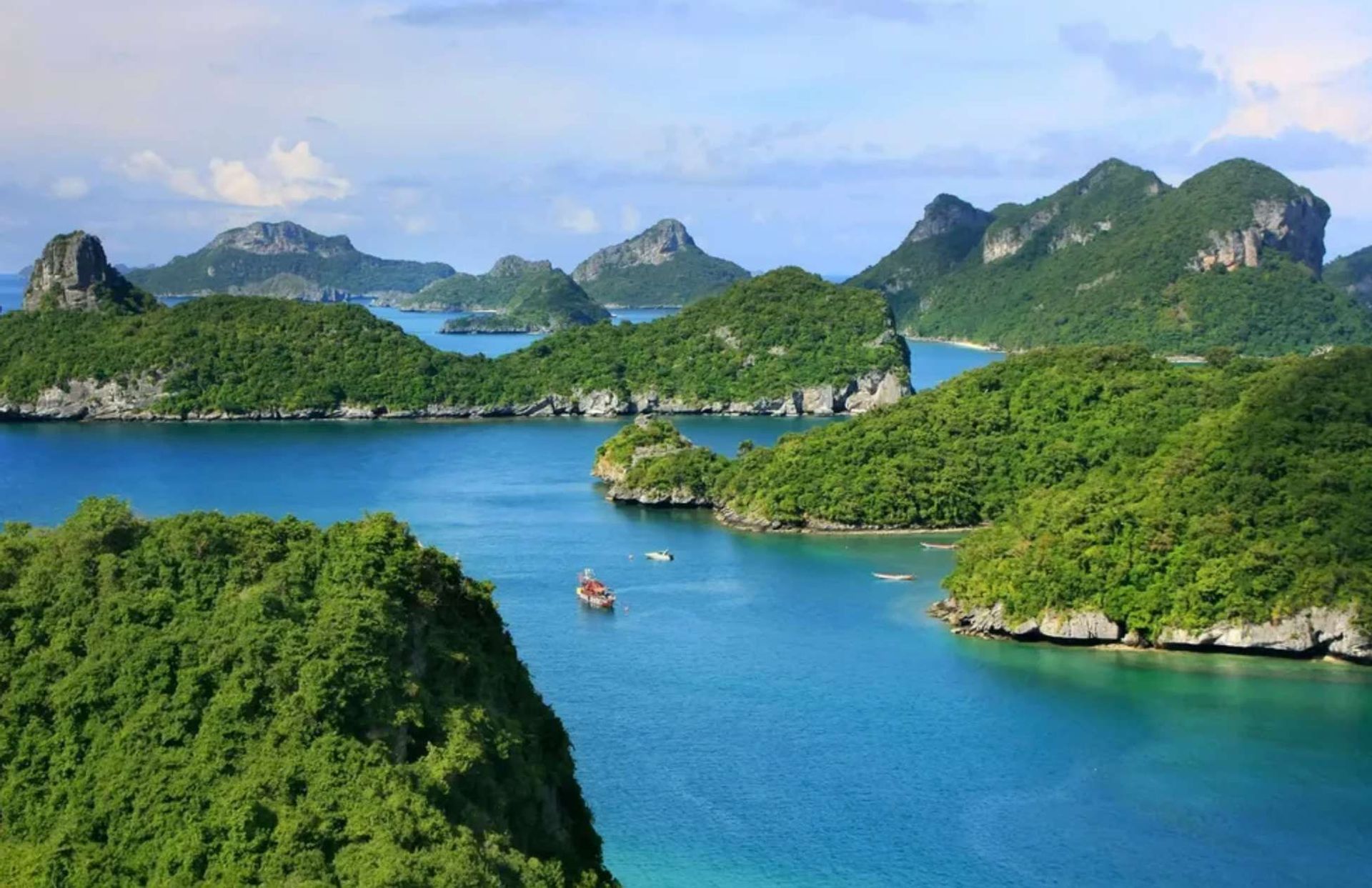 Une vue panoramique de nombreuses îles verdoyantes et luxuriantes, émergeant d'une mer bleue calme, avec quelques petits bateaux sur l'eau.