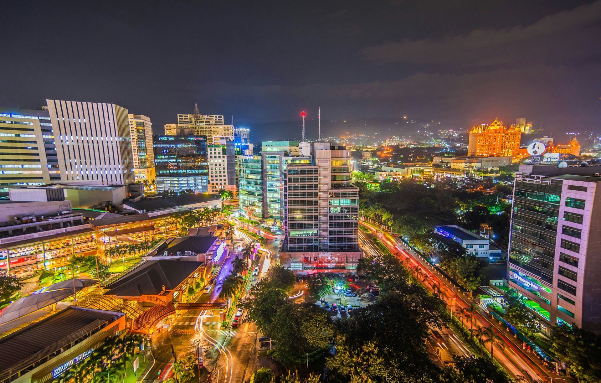Vista panoramica di una città animata di notte, con edifici illuminati e scie luminose del traffico a lunga esposizione.