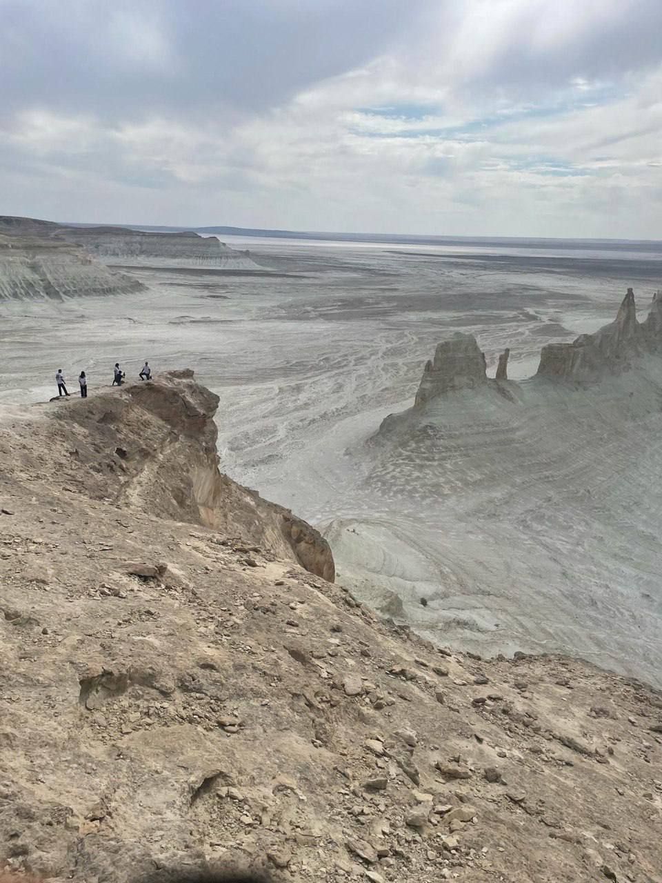 Un gruppo WeRoad di quattro persone in piedi sul bordo di una scogliera rocciosa, affacciato su un vasto canyon arido con guglie di roccia sotto un cielo nuvoloso.