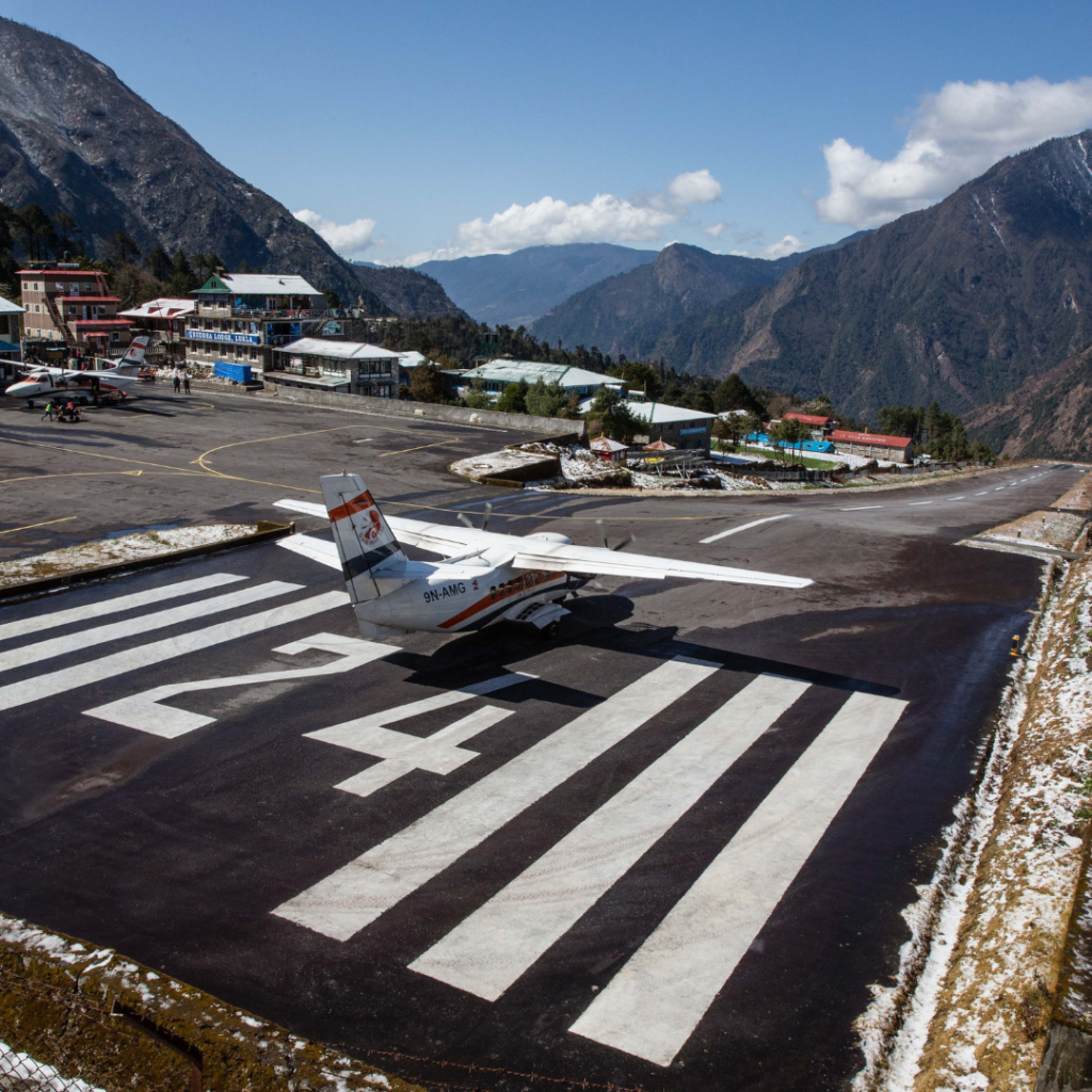 Un petit avion à hélice sur une piste marquée du numéro 24, situé dans une vallée montagneuse d'altitude avec des bâtiments à proximité.
