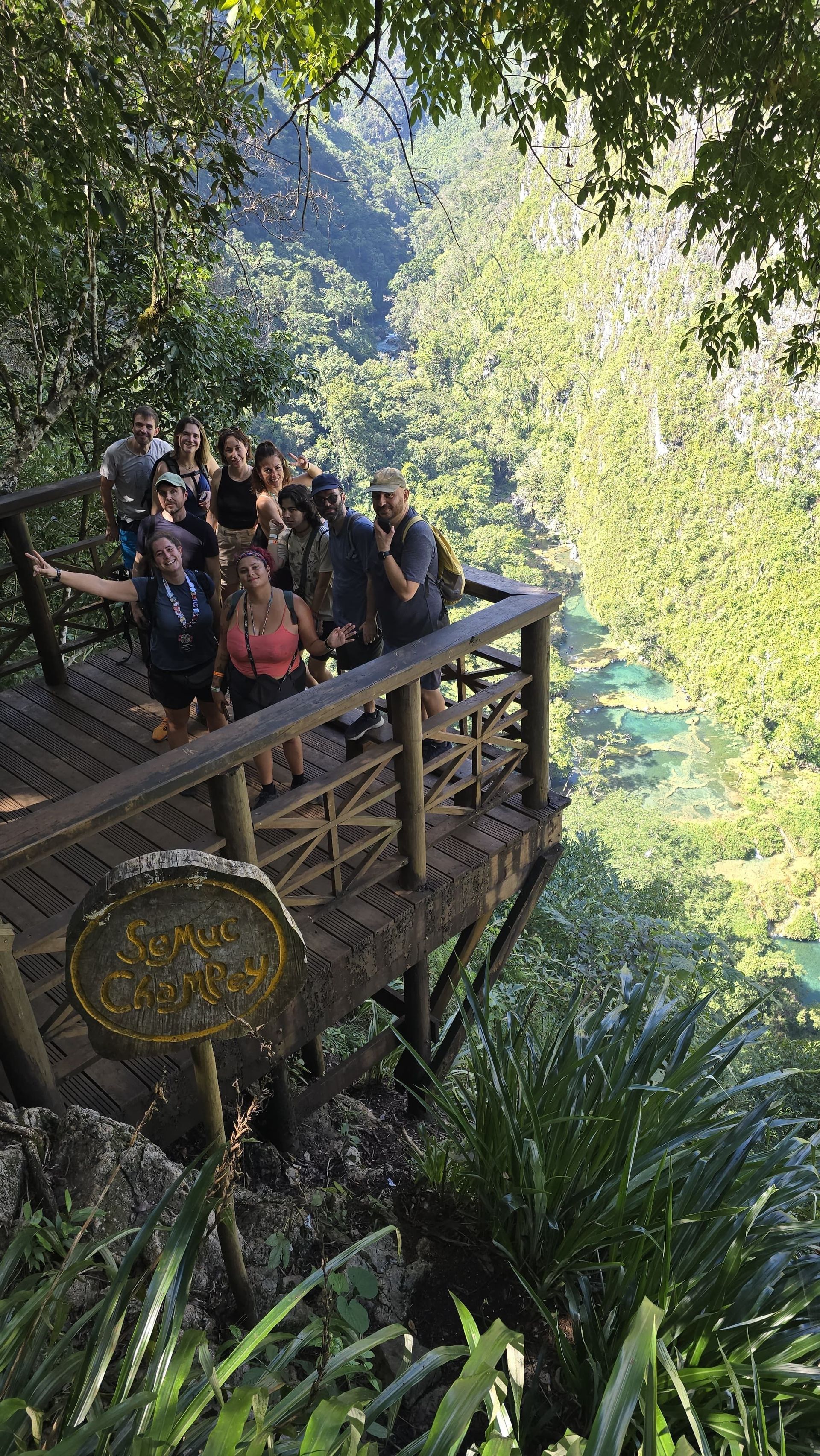 Un groupe WeRoad en photo sur un point de vue en bois, surplombant une vallée verdoyante et une rivière turquoise.