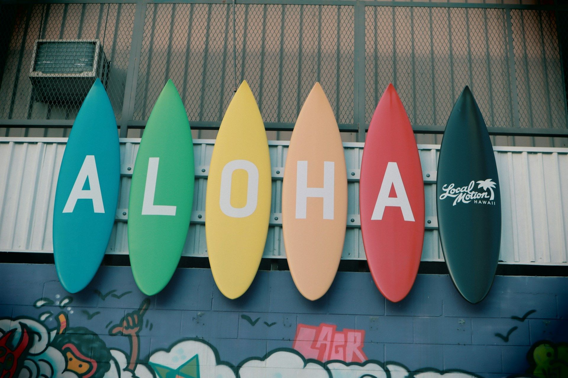 Six colorful surfboards mounted in a row on a wall, spelling out the word ALOHA.