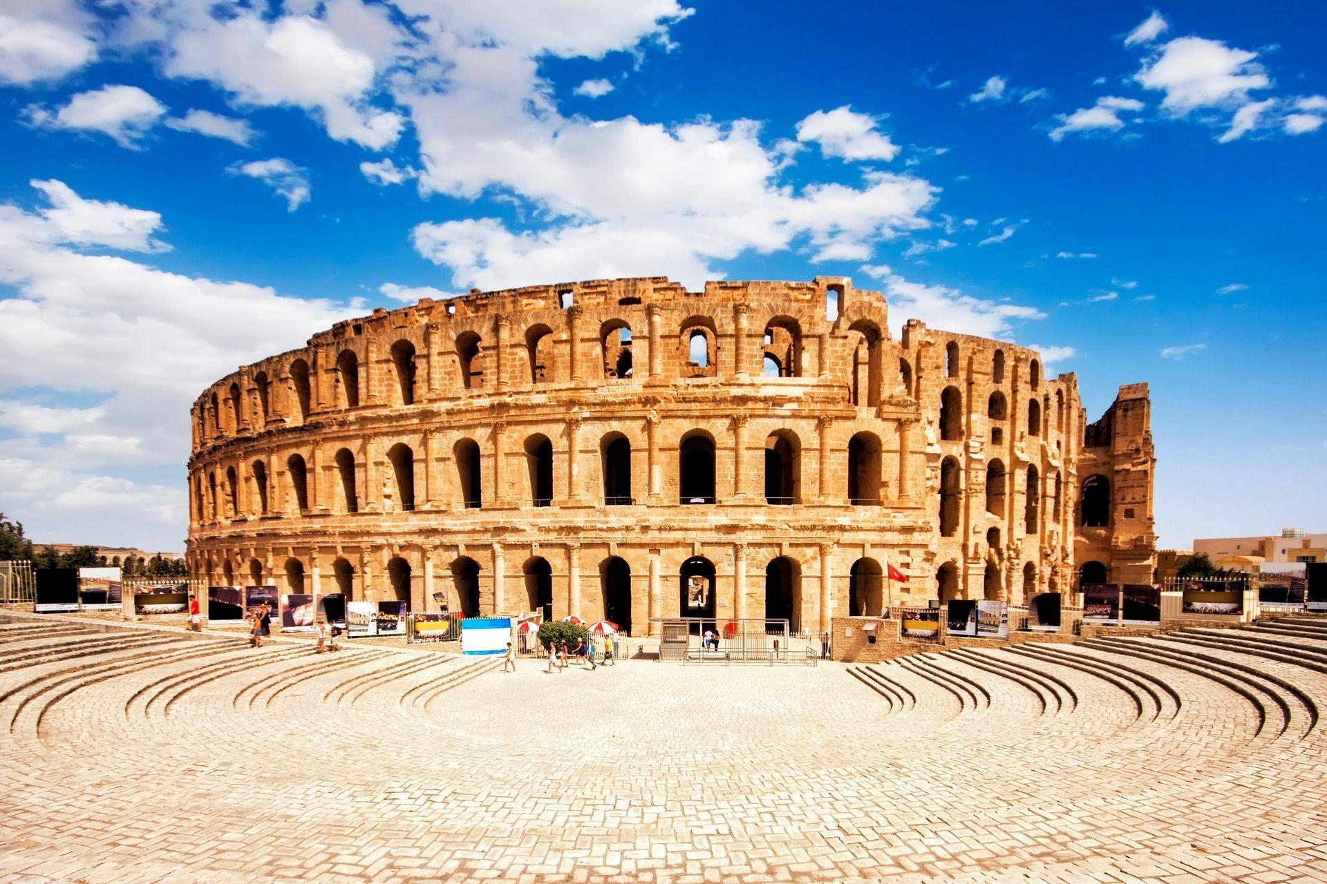 Die Ruinen eines großen, runden Steinamphitheaters stehen unter blauem Himmel mit weißen Wolken, mit Menschen im Vordergrund.