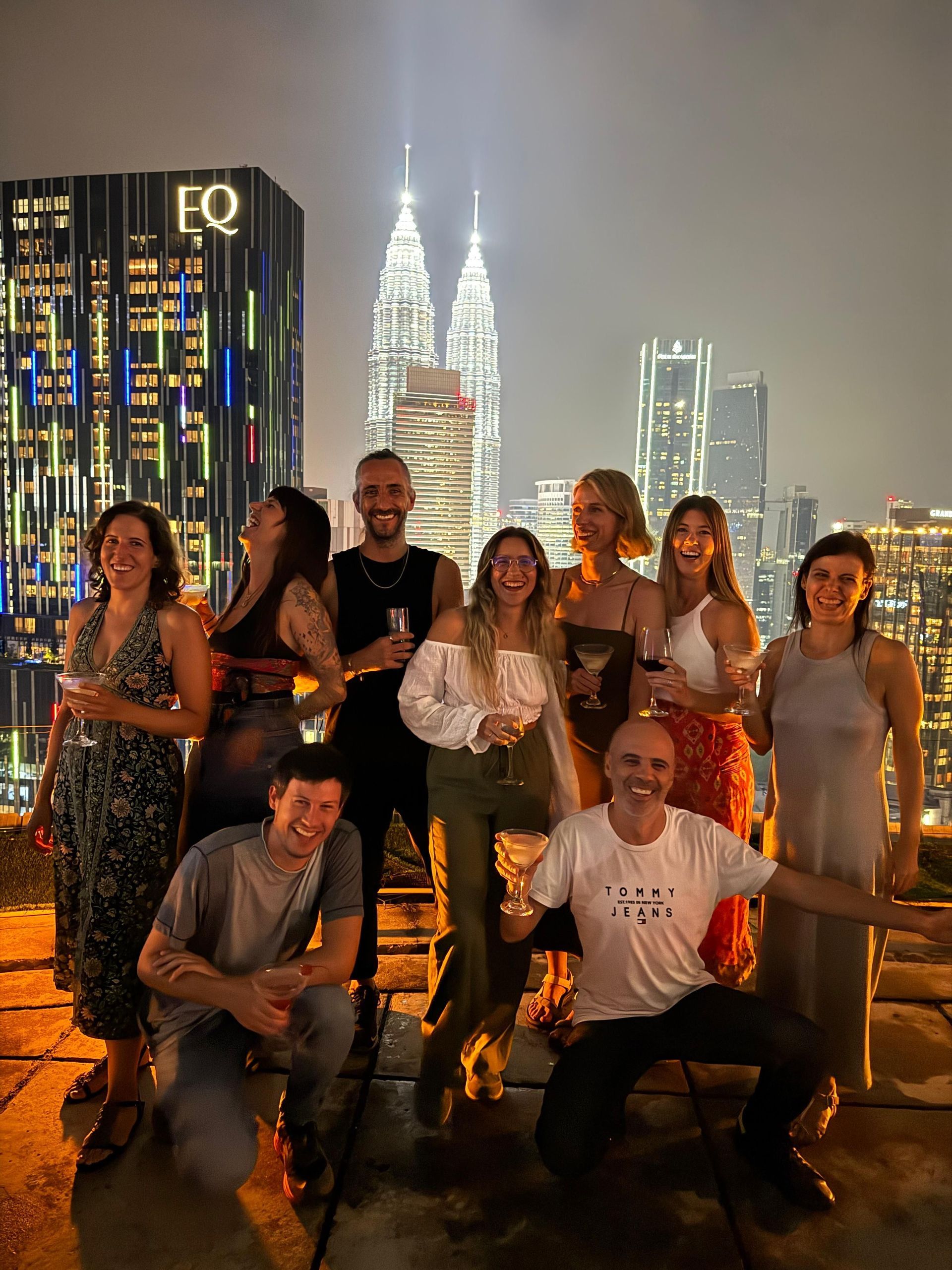 Un grupo de WeRoad sonríe y posa con bebidas en una azotea de noche, con el horizonte de una ciudad iluminada de fondo.