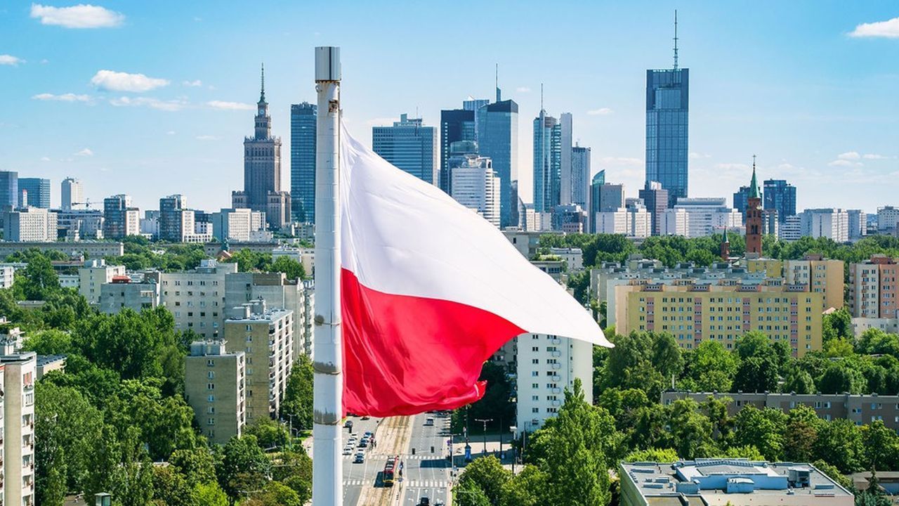 Le drapeau de la Pologne flotte au premier plan avec une ligne d'horizon moderne de la ville, composée de gratte-ciel et d'arbres verts luxuriants en arrière-plan.