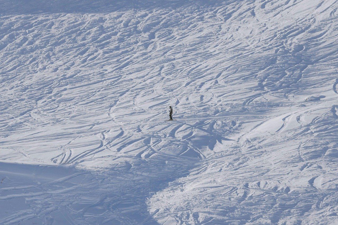 Uno snowboarder solitario su un vasto pendio innevato e tracciato.