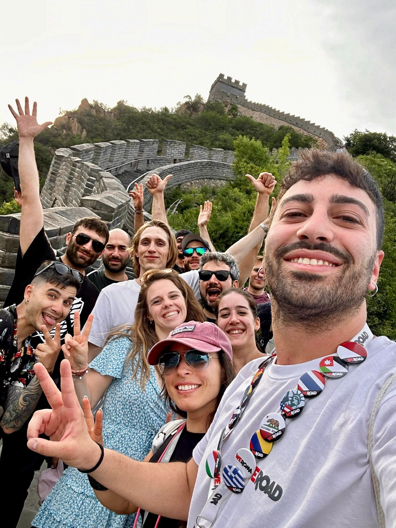 Un gruppo WeRoad sorride e si mette in posa per un selfie su una grande cinta muraria storica che si snoda in un paesaggio verde e collinare.