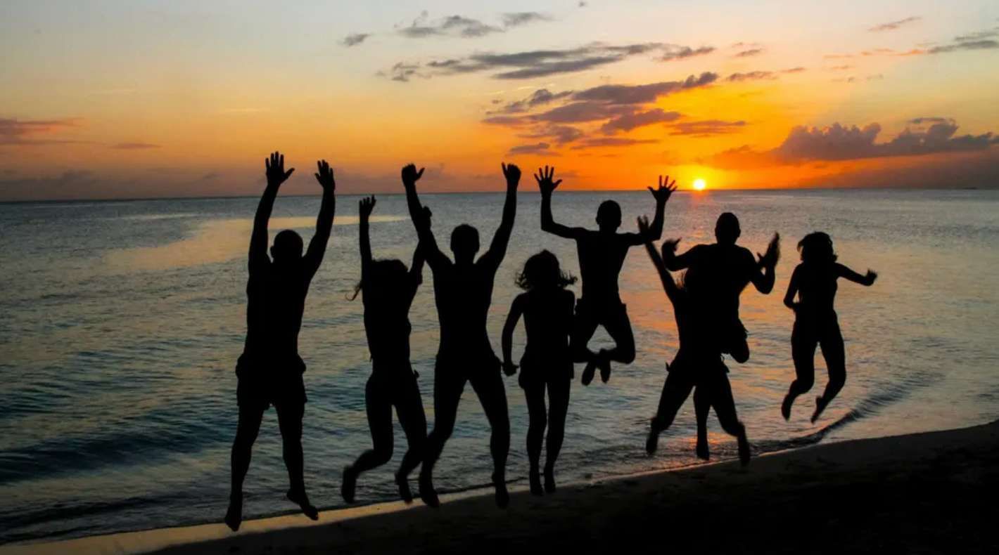 Un voyage de groupe WeRoad en silhouette devant un coucher de soleil orange, sautant ensemble sur une plage au bord de la mer.
