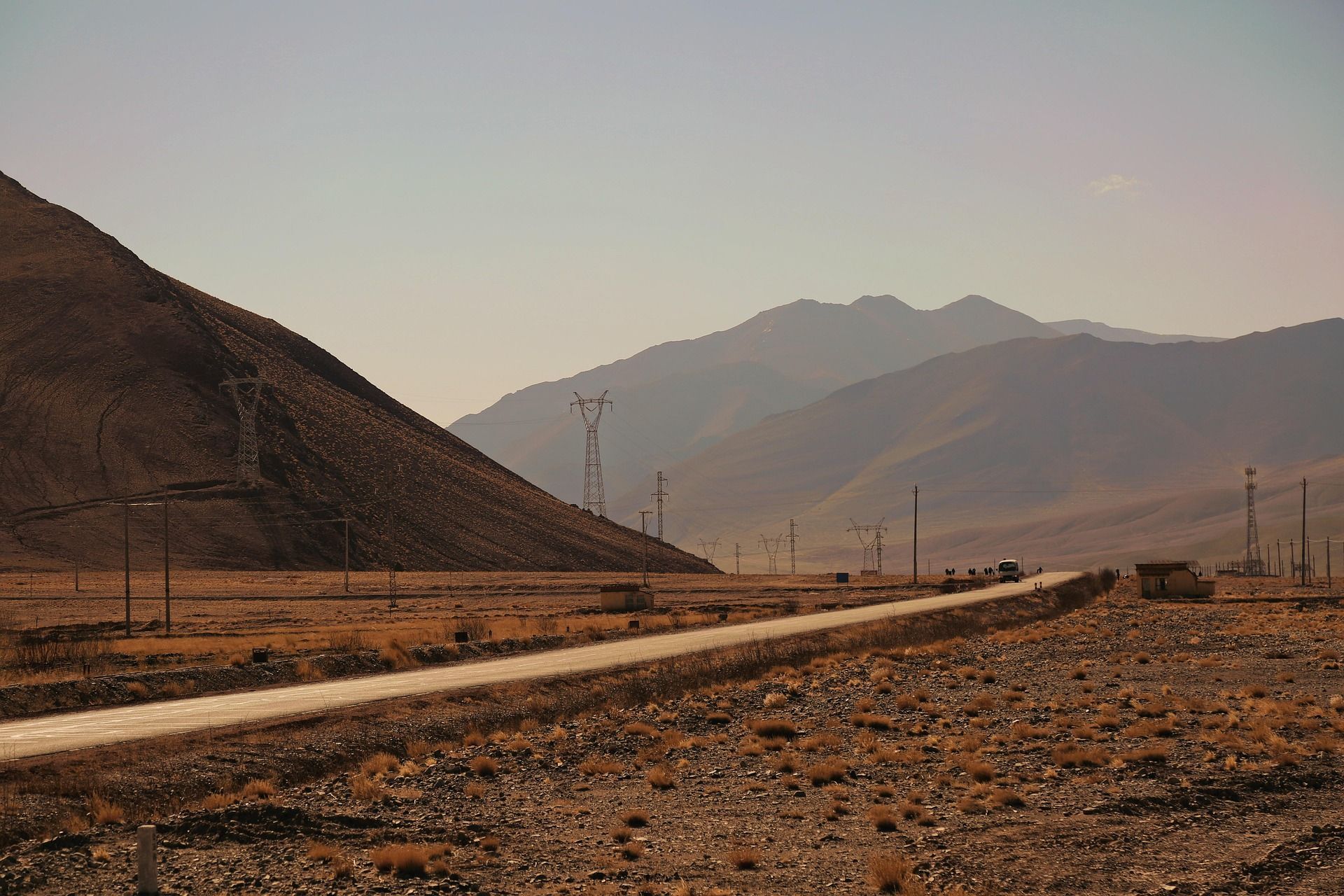 Un viaggio di gruppo WeRoad in autobus è fermo su una lunga strada che attraversa un vasto e arido paesaggio montuoso, con tralicci dell'alta tensione.