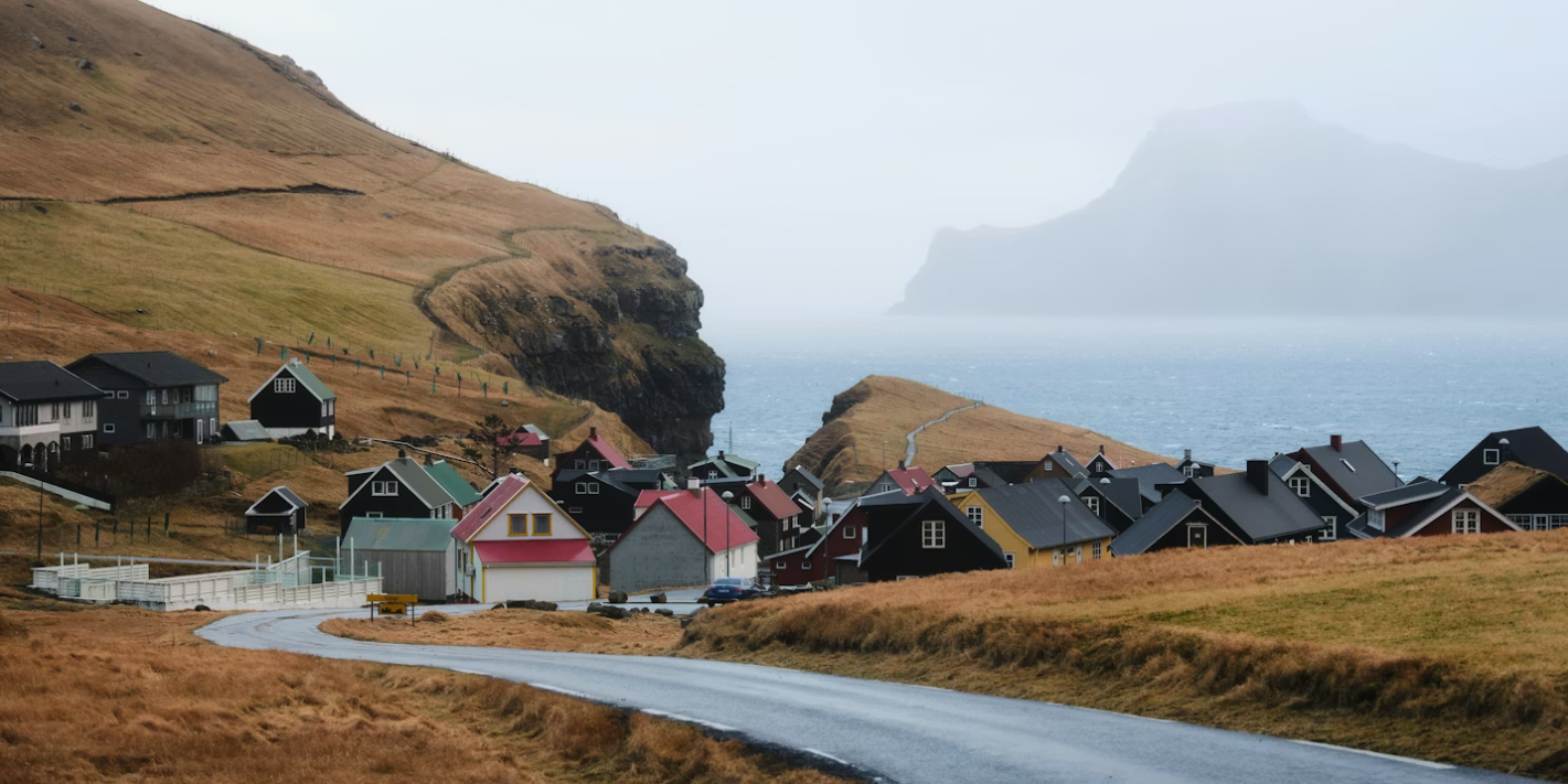 Un petit village côtier aux maisons colorées nichées à flanc de colline verdoyante, au bord d'un vaste océan par une journée nuageuse.
